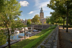 Zonnig uitzicht op de historische haven van Zutphen met aangemeerde boten en de imposante Walburgiskerk op de achtergrond, omringd door groene bomen en karakteristieke oude gebouwen – historic harbor, boats, and St. Walburgis church in Zutphen, the Netherlands